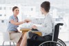 Businesswoman shaking hands with disabled colleague at desk in o