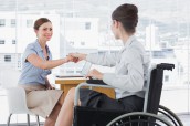 Businesswoman shaking hands with disabled colleague at desk in o