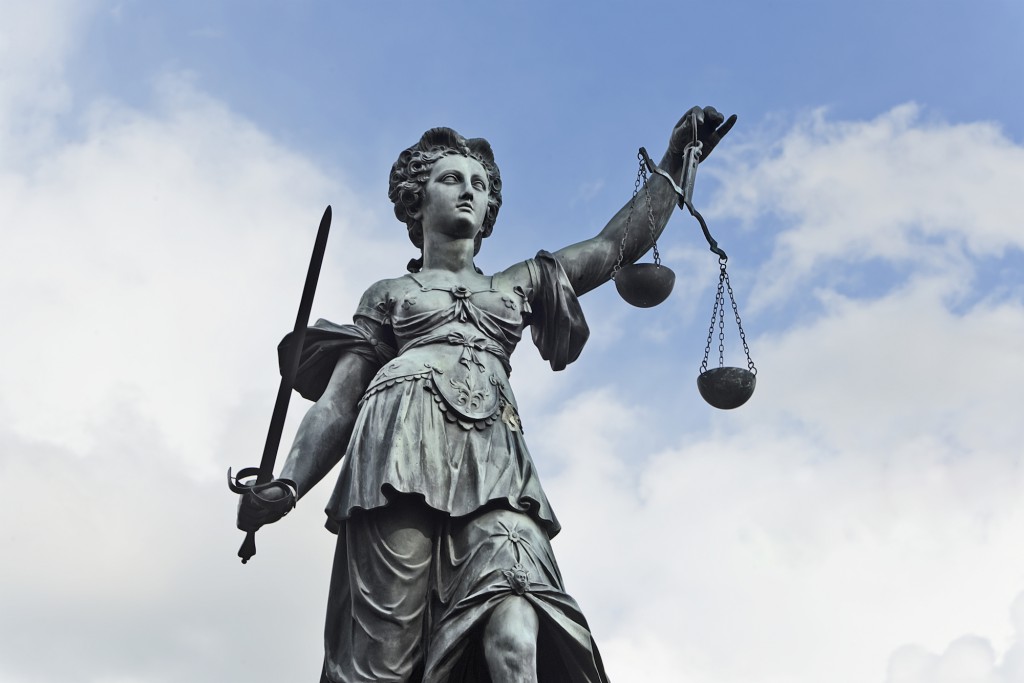 Statue of Justice with sword and scales in front of a blue cloudy sky