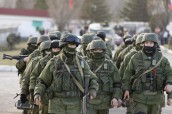 Military personnel, believed to be Russian servicemen, walk outside the territory of a Ukrainian military unit in the village of Perevalnoye outside Simferopol