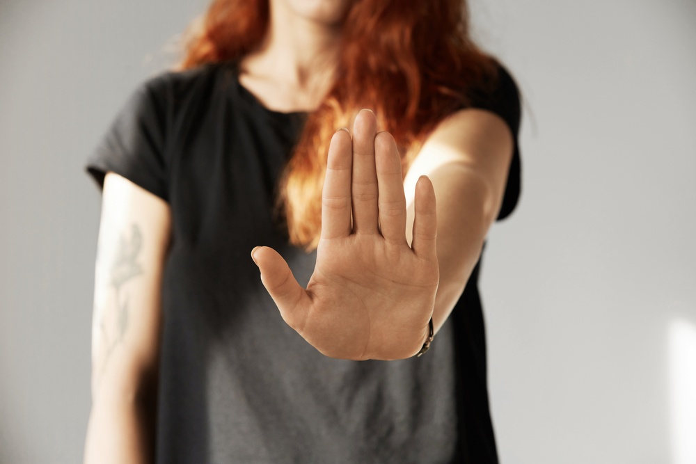 Cropped isolated view of young woman with red hair making stop gesture with her palm. Portrait of teenager girl wearing black T-shirt showing stop sign while arguing with her parents. Body language