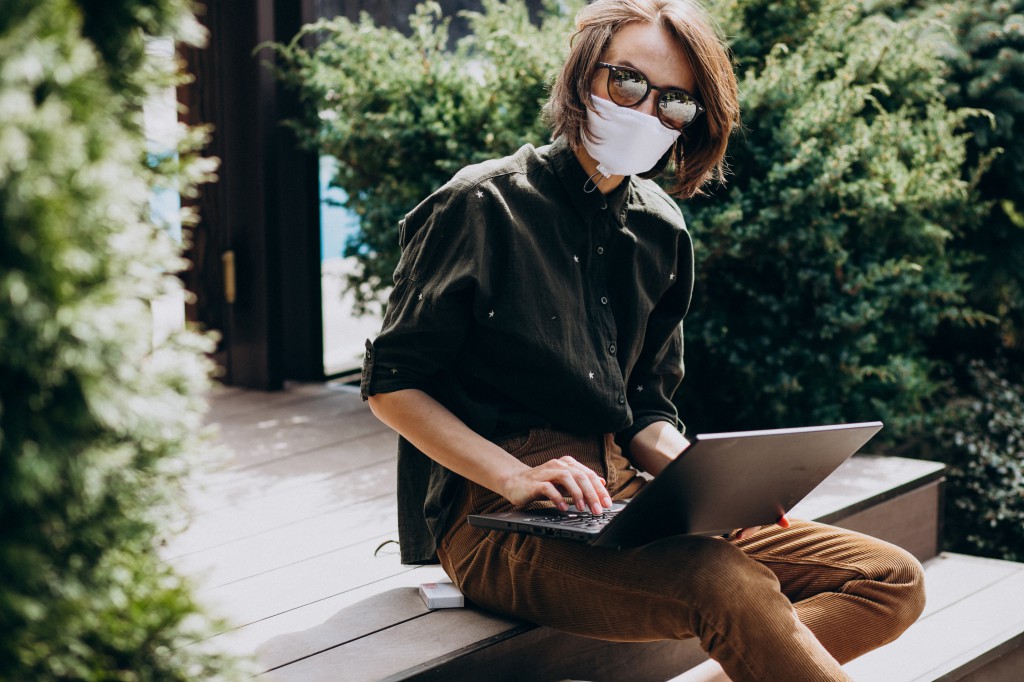 Young business woman working on computer from home in mask