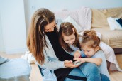 Mom and two daughters are looking at the smartphone