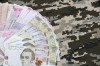 Ukrainian hryvnya bills on fabric with texture of Ukrainian military pixeled camouflage. Cloth with camo pattern in grey, brown and green pixel shapes