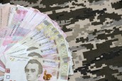Ukrainian hryvnya bills on fabric with texture of Ukrainian military pixeled camouflage. Cloth with camo pattern in grey, brown and green pixel shapes