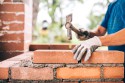 industrial worker building exterior walls, using hammer for laying bricks in cement. Detail of worker with tools